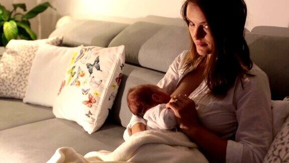 年轻美丽的母亲在昏暗的灯光下给她的新生儿喂奶妈妈母乳喂养婴儿