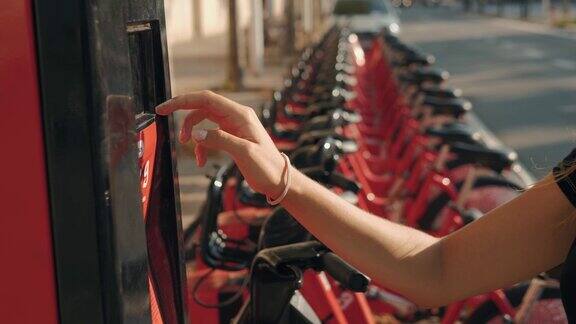排在自行车架上的红色自行车在巴塞罗那的街道上可供出租女孩拿着自行车用手机刷卡申请