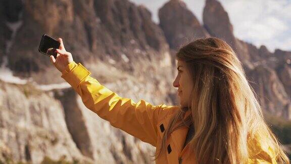 年轻开朗的女人穿着黄色雨衣自拍在美丽的山背景在阳光明媚的一天慢镜头