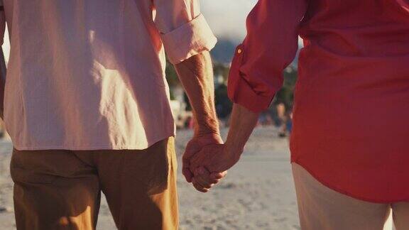 一对老年夫妇手牵着手在海滩上散步