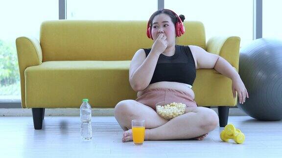 大块头女人听音乐和亚洲女孩喜欢在家里的沙发上吃食物