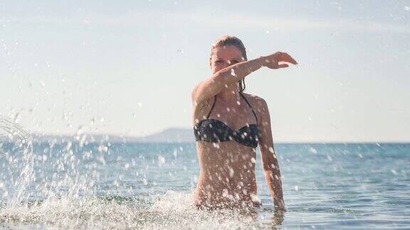 在一个炎热的阳光灿烂的日子里一个女人在海滩上享受夏天站在大海里对着镜头溅起海水