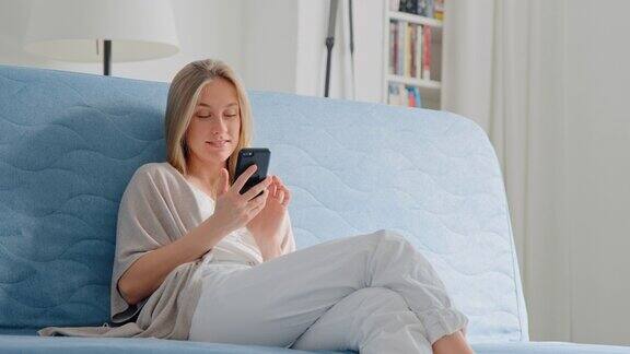 年轻漂亮的女人在家里的沙发上使用智能手机