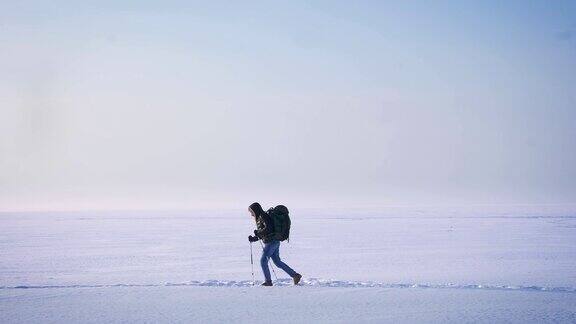 宽阔的镜头疲惫的背包客的剪影在侧面行走与山手杖向左在雪地上