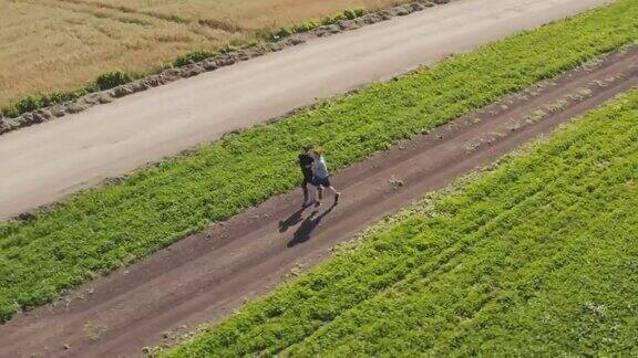 一个年轻的男子和一个女孩在绿色和谷物田旁边的一条土路上慢跑