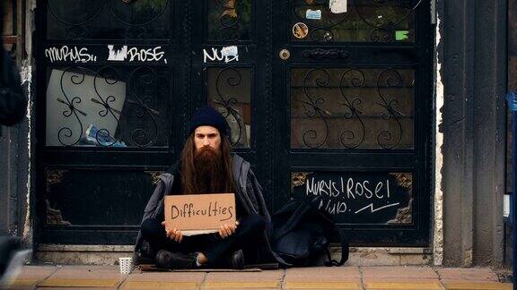 无家可归的人拿着“困难”纸板在拥挤的街道上乞讨