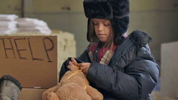 一个疲倦的无家可归的孩子穿着脏衣服试图用冻僵的手给泰迪熊系一个蝴蝶结
