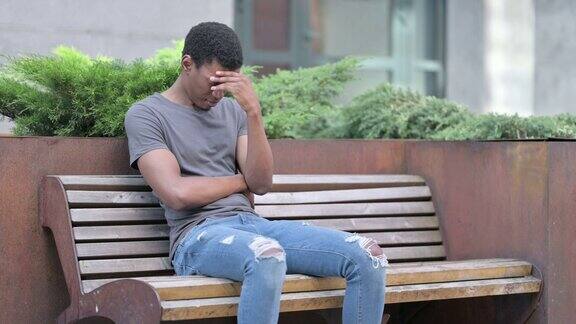 担忧的年轻非洲人坐在长椅上思考