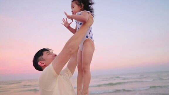 亚洲父亲抱着女儿在空中而散步在海滩上的黄昏时间度假