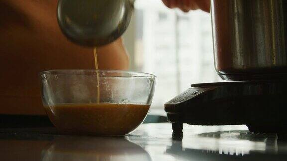 在一个商业厨房里一个人把番茄汤从一个放在电炉上的不锈钢炖锅舀到一个小的玻璃碗里