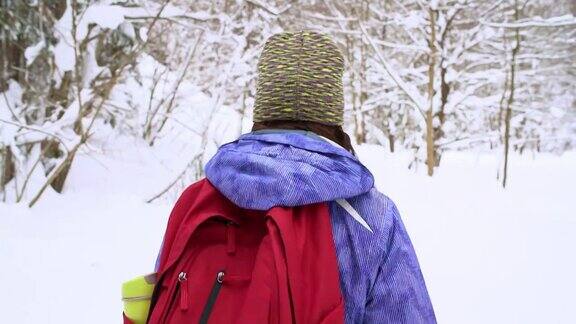 一名女子背着背包穿过白雪覆盖的森林的慢镜头