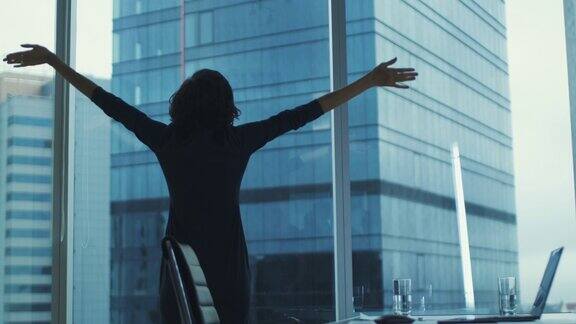 女商人在落地窗前看着城市大楼伸展手臂
