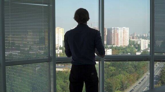 一个年轻人面对窗户站着正在讲电话
