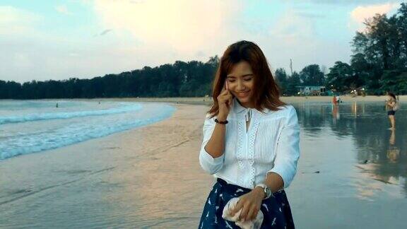 亚洲年轻女子在海滩上散步时给一个电话