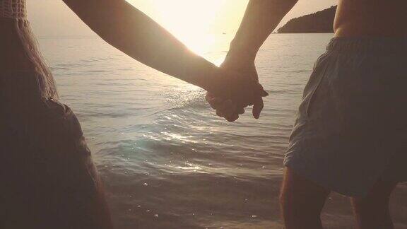 情侣们手牵着手在夕阳下的海滩上走在海水里