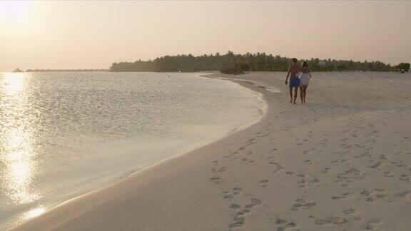 马尔代夫一对情侣在日落时分漫步在宁静的热带海滩上