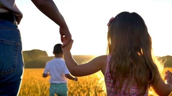 夏日里母亲牵着女儿的手带着孩子的剪影走在田野的阳光下家庭观念