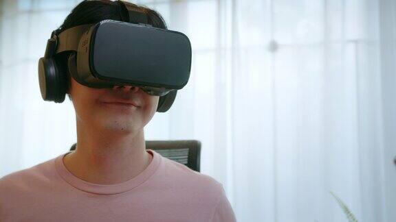 亚洲男子戴着虚拟现实眼镜头戴着头盔看电影和玩视频游戏VR头戴在家里看360度视频晕动病混合现实技术虚拟购物