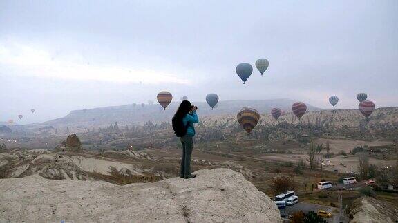 在土耳其卡帕多西亚的戈雷米一个年轻的摄影师正在拍摄热气球飞行的照片