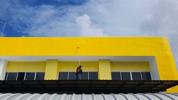 油漆工手动滚动黄色颜料在墙上蓝色的天空背景