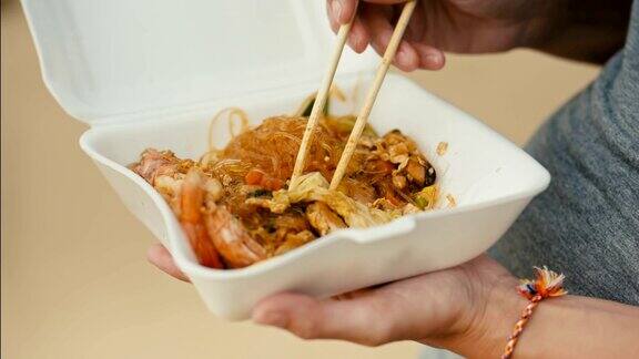 一个女人用筷子在外卖盒里吃亚洲炒面
