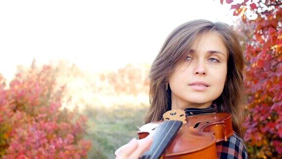 慢镜头美丽的女子在红色秋叶的背景下享受着小提琴的演奏面对着从事音乐艺术的浪漫女孩对自然的表演对爱好