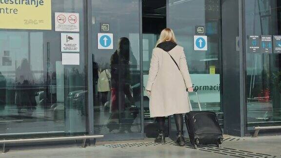 一位女士带着行李进入机场的滑动玻璃门