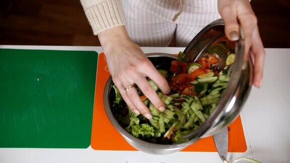 那位妇女把沙拉倒在碗里在厨房里准备蔬菜沙拉