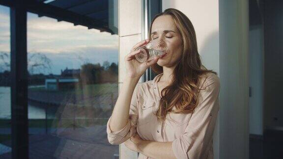 放松的女人喝着水靠近全景窗口口渴的女士喝水