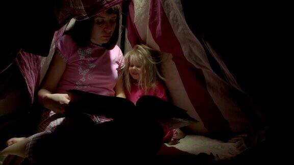 妈妈和女儿晚上在帐篷里用手电筒看书
