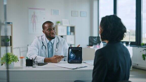 一名年轻黑人医生在健康诊所的平板电脑上向病人展示乳房x光检查结果友善助理讲解预防乳腺癌筛检的重要性