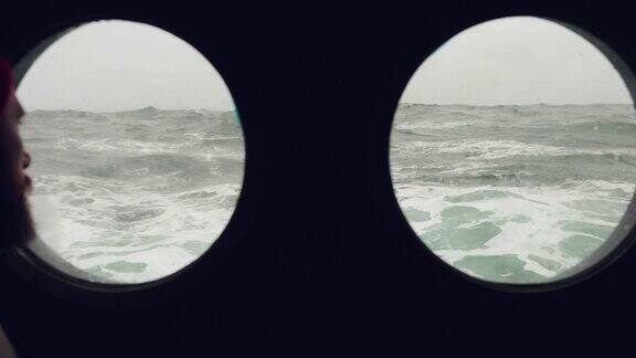 在波涛汹涌的海面上一名长胡子的水手站在一艘船的舷窗前