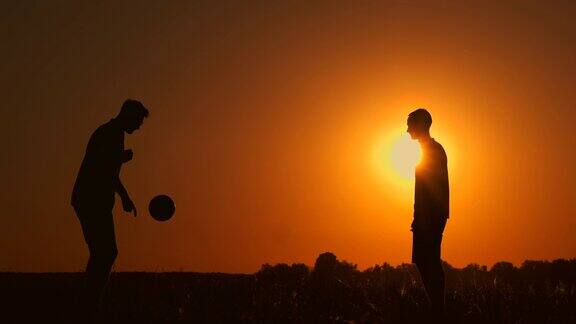 两个男孩在日落时踢足球日落时孩子们玩球的剪影幸福家庭