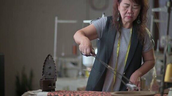 亚洲中国高级妇女裁缝拿起滚烫的木炭从陶器与服务钳放入古董铁传统熨烫