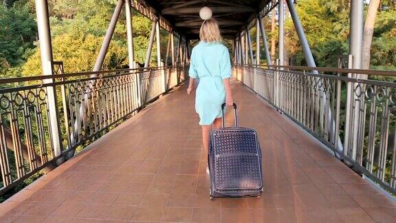 美丽的女人带着行李离开酒店走在度假城市的街道上