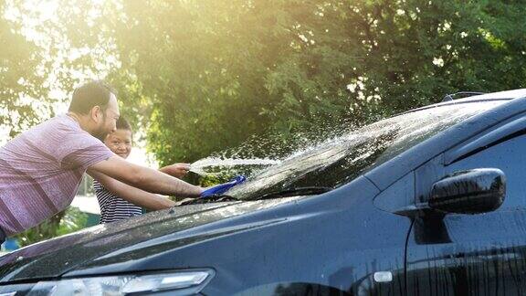 快乐的亚洲男孩帮助父母洗车在洒水与阳光在家里慢镜头家庭活动假期