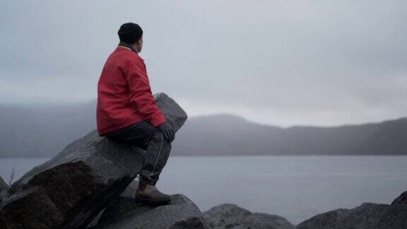 徒步旅行者坐在迷雾峡湾旁的岩石上