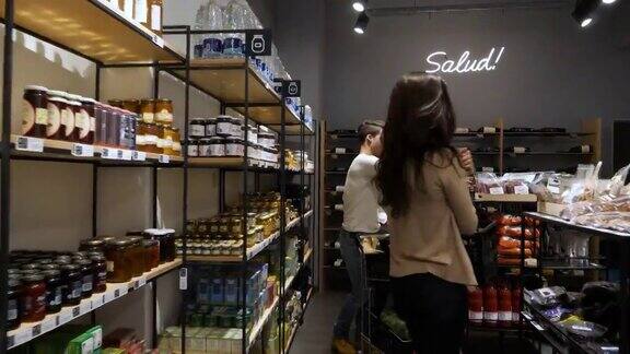 在有机食品商店的顾客看着货架和选择的产品看起来非常高兴和微笑