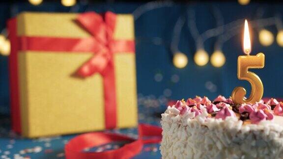 白色生日蛋糕5号金色蜡烛用打火机点燃蓝色背景用彩灯和黄色礼盒用红丝带绑起来特写镜头