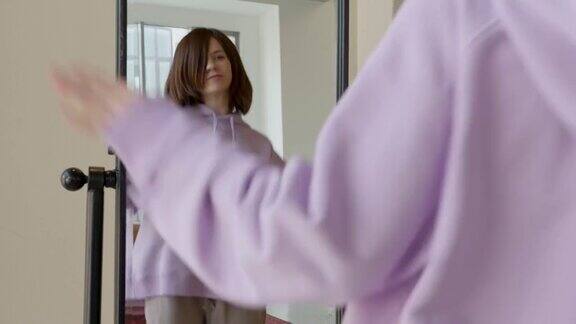 一个女人穿着紫色连帽衫在镜子前跳舞面带微笑