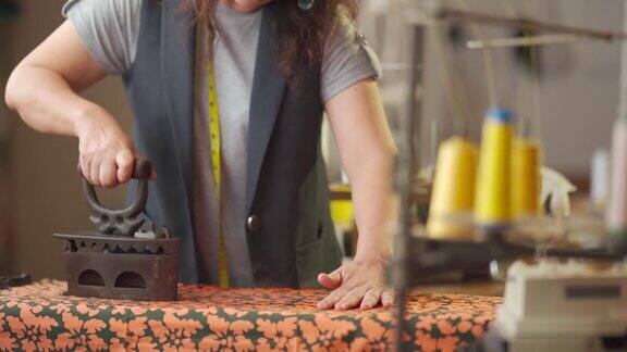 近距离拍摄亚洲华人高级妇女裁缝手用传统古玩铁器具在她的工作室熨布