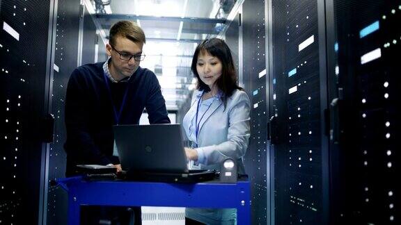 高加索男性和亚洲女性服务器工程师与碰撞车笔记本电脑在大数据中心满机架服务器