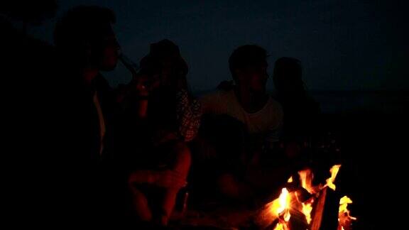 年轻人晚上在海滩上用篝火野餐欢快的朋友们唱着歌弹着吉他Slowmotion拍摄