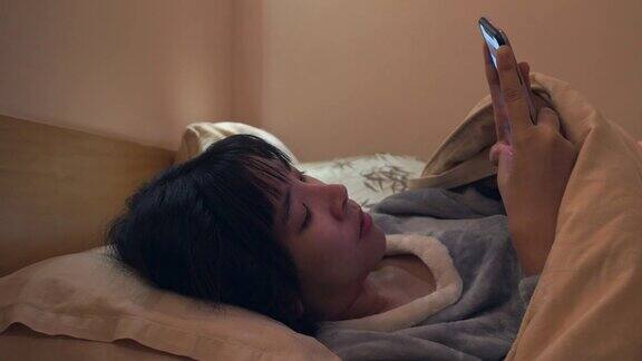 一个亚洲女人在晚上的卧室里用手机发短信