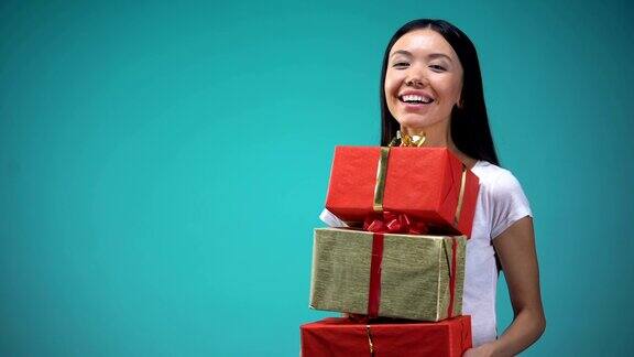 微笑的女孩拿着许多礼盒节日的礼物站在蓝色的背景