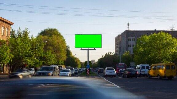 一个绿色屏幕的广告牌背景是城市交通汽车行人树木蓝天在亚美尼亚城市埃里温摄像机移开了
