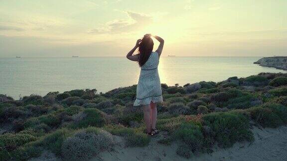 一个年轻女子站在海面上看着夕阳