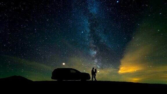 一个男人和一个女人站在一辆汽车旁映衬着星空时间流逝