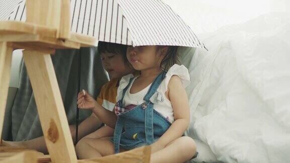 泰国可爱的小女孩在伞下一边吃糖果一边和她的弟弟跳舞