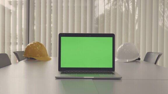 现场拍摄的笔记本电脑显示绿色色度键屏幕站在办公室与工程安全帽技术在背景技术背景